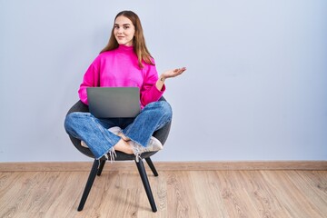 Canvas Print - Young hispanic girl working using computer laptop smiling cheerful presenting and pointing with palm of hand looking at the camera.