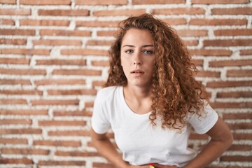 Poster - Young caucasian woman standing over bricks wall background with hand on stomach because indigestion, painful illness feeling unwell. ache concept.