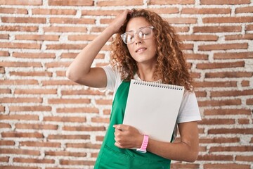 Poster - Young caucasian woman holding art notebook smiling confident touching hair with hand up gesture, posing attractive and fashionable