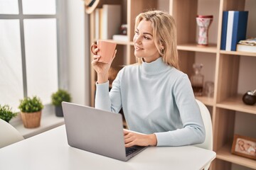 Sticker - Young blonde woman using laptop and drinking coffee sitting on table at home