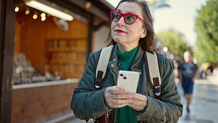 Sticker - Mature hispanic woman with grey hair tourist wearing backpack using smartphone at street market