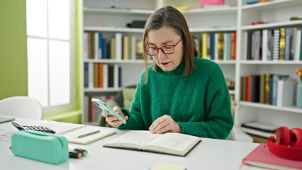 Poster - Mature hispanic woman with grey hair student using smartphone reading a book at library