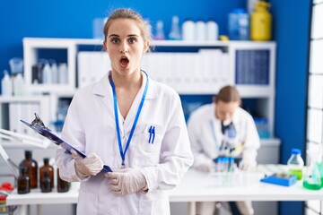 Sticker - Blonde woman working at scientist laboratory scared and amazed with open mouth for surprise, disbelief face