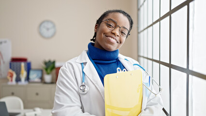 Canvas Print - African american woman doctor smiling confident holding document on clipboard at clinic