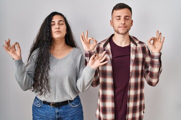 Poster - Young hispanic couple standing over white background relaxed and smiling with eyes closed doing meditation gesture with fingers. yoga concept.