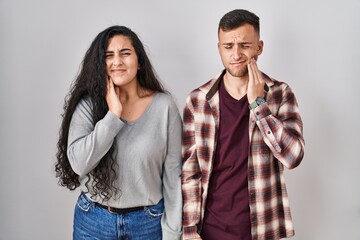 Poster - Young hispanic couple standing over white background touching mouth with hand with painful expression because of toothache or dental illness on teeth. dentist