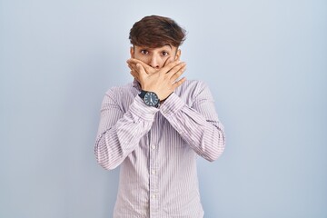 Wall Mural - Arab man with beard standing over blue background shocked covering mouth with hands for mistake. secret concept.