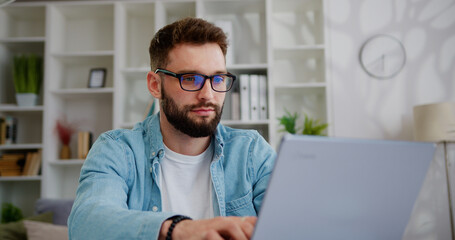 handsome caucasian man working on laptop computer while sitting behind desk in living room. freelanc
