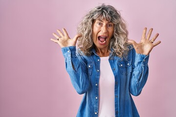 Canvas Print - Middle age woman standing over pink background celebrating crazy and amazed for success with arms raised and open eyes screaming excited. winner concept