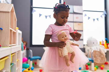 African american girl holding baby doll standing at kindergarten