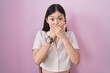 Chinese young woman standing over pink background shocked covering mouth with hands for mistake. secret concept.