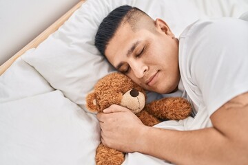 Poster - Young latin man hugging teddy bear lying on bed sleeping at bedroom