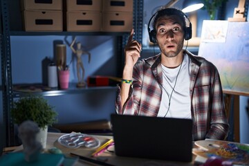 Poster - Young hispanic man sitting at art studio with laptop late at night pointing finger up with successful idea. exited and happy. number one.