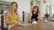 © Krakenimages.com - Two women using laptop writing on notebook sitting on table at home terrace