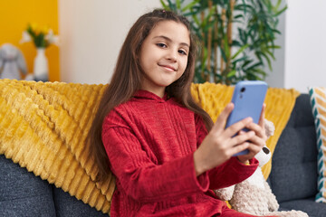 Sticker - Adorable hispanic girl using smartphone sitting on sofa at home