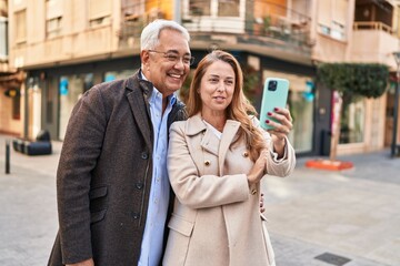 Wall Mural - Middle age man and woman couple smiling confident having video call at street