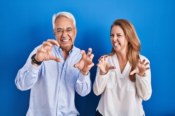 Sticker - Middle age hispanic couple standing over blue background smiling funny doing claw gesture as cat, aggressive and sexy expression