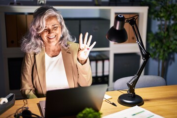 Poster - Middle age woman with grey hair working using computer laptop late at night showing and pointing up with fingers number four while smiling confident and happy.