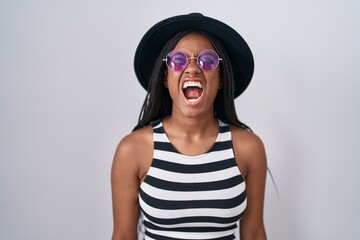 Poster - Young african american with braids wearing hat and sunglasses angry and mad screaming frustrated and furious, shouting with anger. rage and aggressive concept.