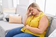 Young woman sitting on sofa suffering for head and stomach ache at home