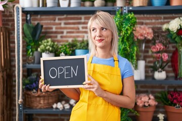 Poster - Young caucasian woman working at florist holding open sign smiling looking to the side and staring away thinking.