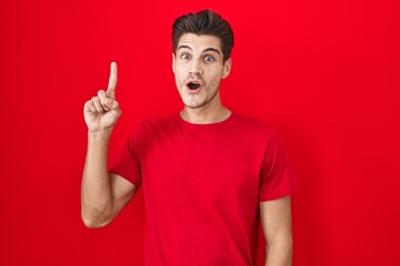 Poster - Young hispanic man standing over red background pointing finger up with successful idea. exited and happy. number one.