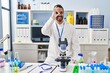 © Krakenimages.com - Young hispanic man with beard working at scientist laboratory doing ok gesture with hand smiling, eye looking through fingers with happy face.