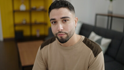 Sticker - Young arab man sitting on sofa with relaxed expression at home