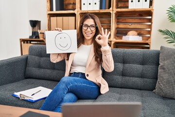 Canvas Print - Young brunette woman on therapy session working at consultation office doing ok sign with fingers, smiling friendly gesturing excellent symbol