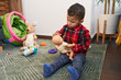 Adorable hispanic boy sitting on floor playing with baby doll at home