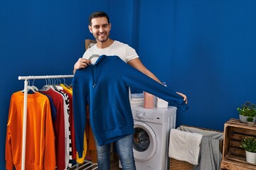 Wall Mural - Young hispanic man putting clothes on clothes rack at laundry room