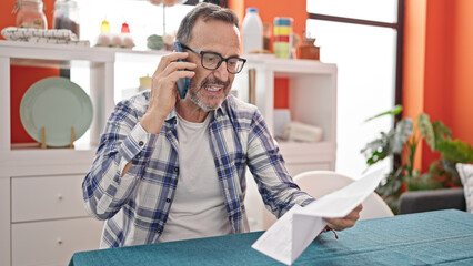 Canvas Print - Middle age man angry reading document talking on smartphone at dinning room