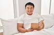 © Krakenimages.com - Young chinese man reading book sitting on bed at bedroom