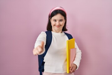 Wall Mural - Woman with down syndrome wearing student backpack and holding books approving doing positive gesture with hand, thumbs up smiling and happy for success. winner gesture.