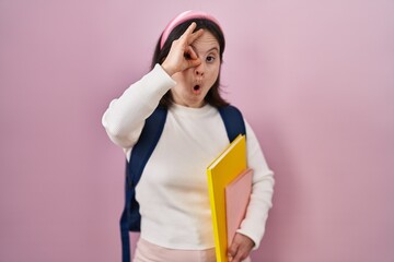 Sticker - Woman with down syndrome wearing student backpack and holding books doing ok gesture shocked with surprised face, eye looking through fingers. unbelieving expression.