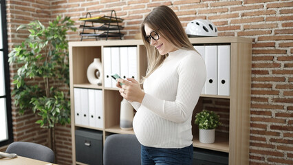 Young pregnant woman business worker using smartphone touching belly at office