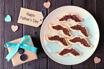 Wall Mural - Fun Fathers Day mustache cookies. Top down view with gift greeting card over a dark wood background.