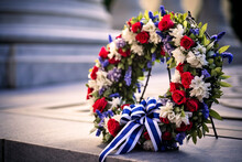 Wreath Made Of Red, White, And Blue Flowers And Ribbons, Resting Against The Base Of A Solemn War Memorial.