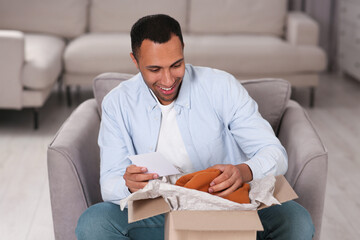 Wall Mural - Happy man with greeting card near parcel at home. Internet shopping