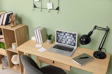 Poster - Modern laptop, books, lamp and stationery on wooden desk near green wall. Home office