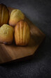 Freshly baked madeleine cakes on a wooden plate and dark table