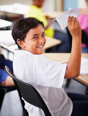 Portrait, student and paper plane in classroom and happy, learning at desks or Indian boy, play and origami jet or class distraction. Playful smile, kid and holding airplane and middle school fun