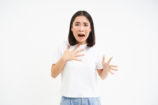 Image of scared asian woman, looking worried and concerned, terrified shouting, standing over white background
