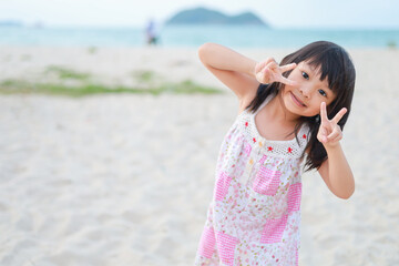 Wall Mural - Portrait​ image​ of​ baby 5-6 years​ old​. Happy Asian child girl playing sand on the beach at the sea. In the summer season.