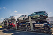 © romaset - Car carrier trailer transports cars on highway at blue sky background.