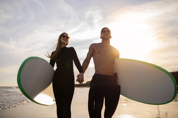 Wall Mural - Romantic Young Couple Walking With Surfboards On Sunset Beach And Holding Hands