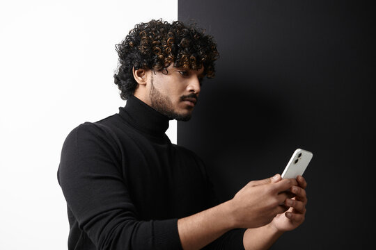 Confident Indian man using smart phone while standing against black and white background
