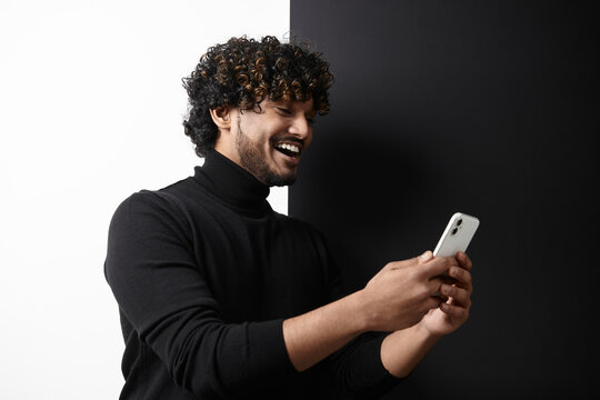 Happy Indian man using smart phone while standing against black and white background
