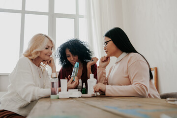 Wall Mural - Three mature women examining beauty products while sitting at the desk together