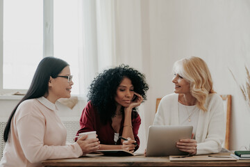 Poster - Three beautiful mature women using digital tablet while sitting at the desk together